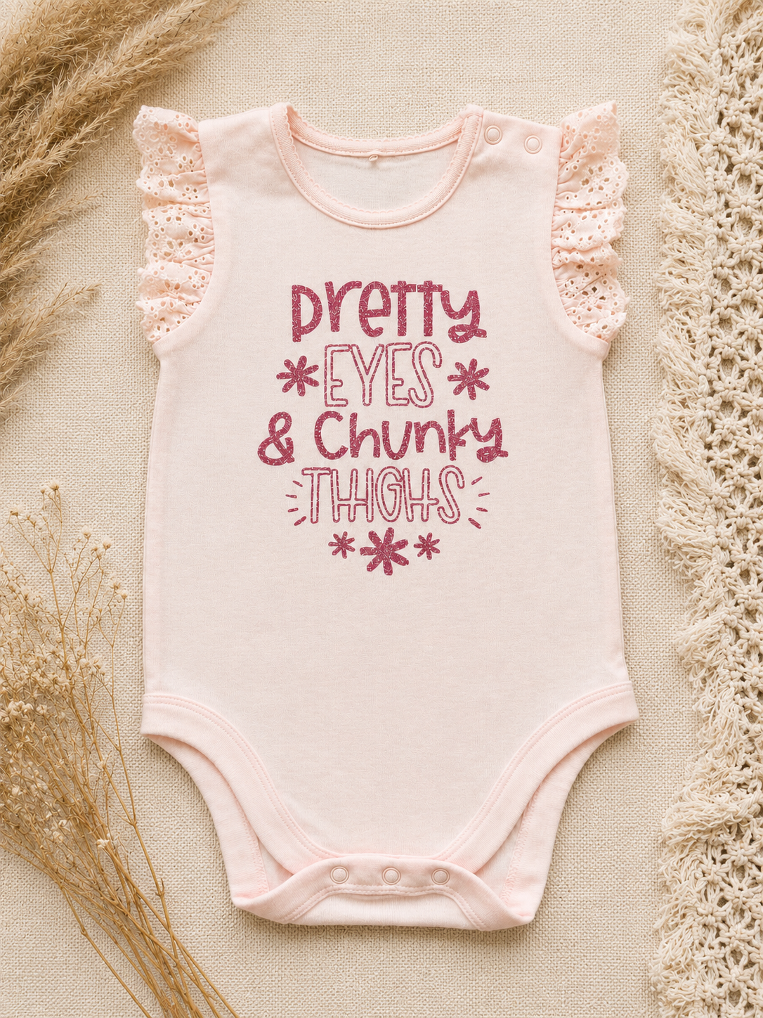 Pink frill sleeve baby bodysuit with Pretty Eyes and Chunky Thighs glitter print laid flat on cream background