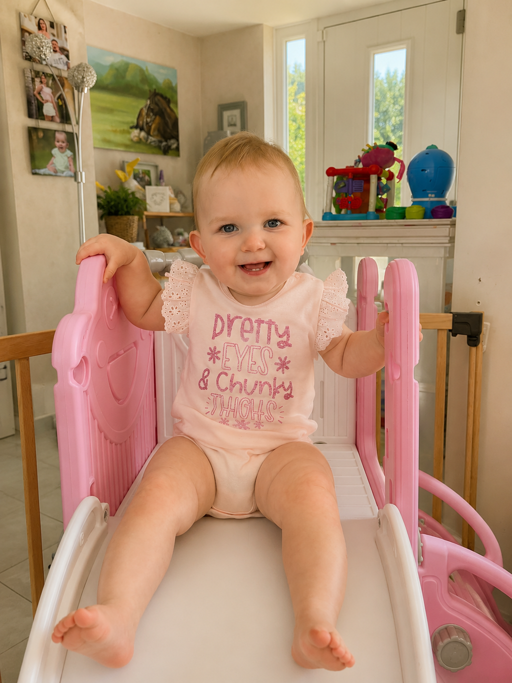 Baby girl sitting in pink slide wearing Pretty Eyes and Chunky Thighs pink frill bodysuit smiling