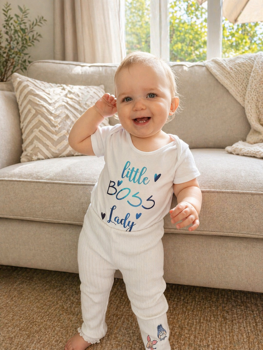 Baby girl standing in living room wearing Little Boss Lady white bodysuit with blue foil print and white ribbed leggings