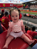 Baby girl wearing pink Formula 1 bodysuit at a race track