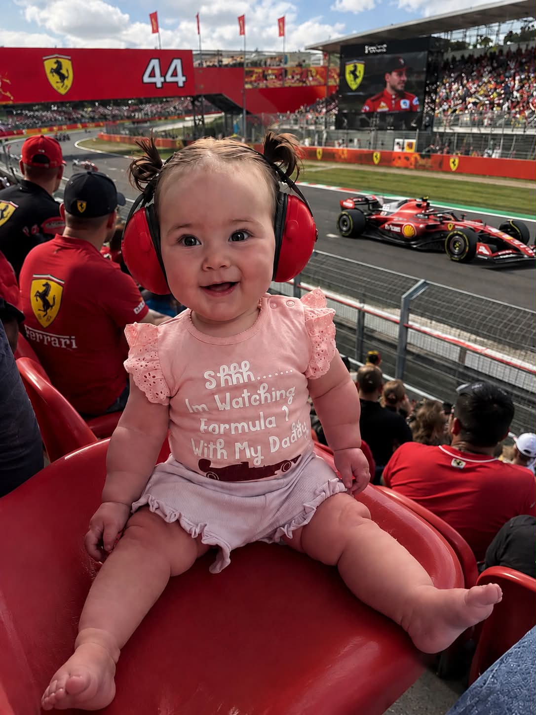 Baby girl wearing pink Formula 1 bodysuit at a race track